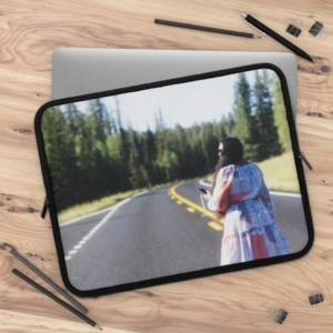 Laptop sleeve displaying woman in colorful striped jacket standing on forest road with evergreen trees.